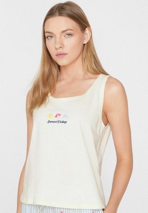 Jeune femme aux longs cheveux blonds portant un haut blanc sans manches avec le texte "Summer Feelings" et de petites icônes de soleil, parapluie et vague.
