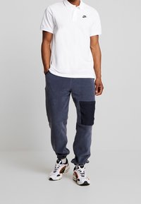 Vit Nike polo, marinblå sweatpants med sidficka och vita sneakers med färgglada detaljer. Avslappnad outfit med en löst sittande passform.