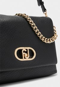Schwarze Lederhandtasche mit einer strukturierten Oberfläche, ausgestattet mit einem goldenen Kettenriemen und einem goldenen ovalen Logoverschluss auf der Vorderseite.
