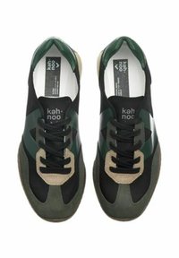 Un paio di sneakers nere, verdi e beige con lacci, con il marchio "kah·noo" sulla linguetta e soletti bianchi con etichette nere del marchio.