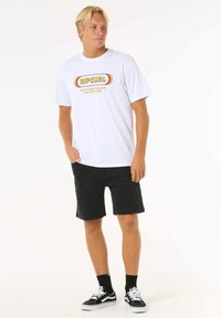 White cotton T-shirt with circular "RIPCURL" logo in orange and yellow, paired with black denim shorts and black sneakers with white soles.