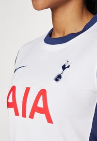 Witte voetbalshirt met korte mouwen, voorzien van een marineblauwe kraag en accentueringen op de mouwen. Groot rood "AIA" logo en geborduurde marineblauwe teamembleem op de borst.