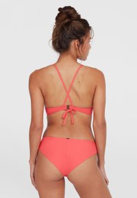 Korálový bikiny set s prekríženým dizajnom na chrbte, nastaviteľnými ramienkami, viazaním a nízkymi nohavičkami, vyrobený z hladkého elastického materiálu.