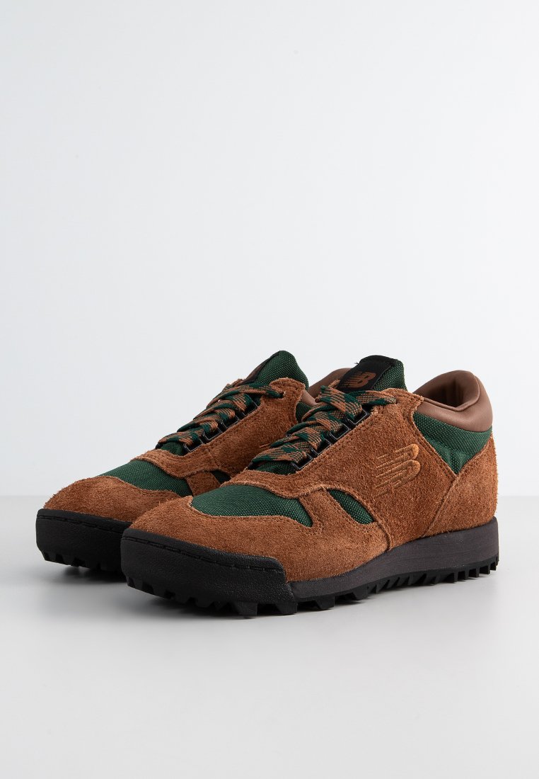 Baskets en daim marron avec des accents en tissu vert, dotées de semelles en caoutchouc noir et de détails en cuir marron au niveau du talon et de la languette.