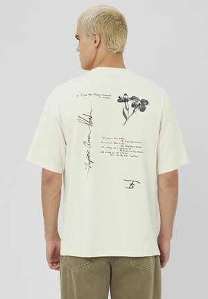 T-shirt en coton cream avec des illustrations florales noires et un texte manuscrit au dos. Manches courtes avec une coupe décontractée.