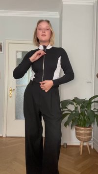 Schwarze Zip-Jacke mit weißen Seitenpaneelen, kombiniert mit hoch taillierten schwarzen weiten Hosen. Glatter Stoff, slim fit, minimalistisches Design.