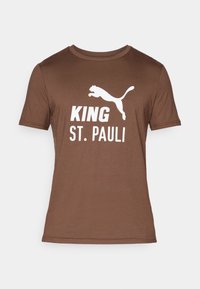 Brun bomulds T-shirt med hvidt grafisk print. Teksten siger "KING ST. PAULI" med en springende panter-logo ovenfor. Korte ærmer, rund hals.