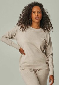 Helle beigefarbene Strickjacke mit Rundhalsausschnitt, gerippten Bündchen und Saum. Verfügt über seitliche Schlitze und ein kleines Logotag am unteren Ende.