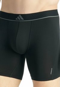 Shorts de compression noirs Adidas portés par une personne, avec un logo gris sur la taille et le texte "AEROREADY" sur la cuisse gauche.