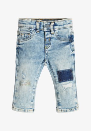 Pantalones de mezclilla de color azul claro con un lavado descolorido, bolsillos delanteros y costuras decorativas. Incluyen un parche de color azul oscuro y detalles desgastados.