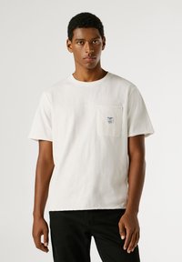 Valge puuvillane T-särk lühikeste varrukatega, ümmargune kaelus ja vasakul rinnal üks tasku, millel on väike sinine silt. Mustad püksid.