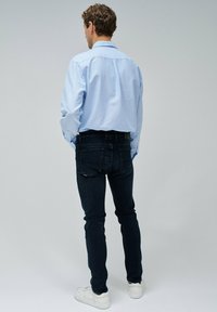 Camisa de botones azul claro, jeans oscuros de corte slim, zapatillas blancas, detalles visibles en la parte trasera, texturas suaves y un ajuste relajado.