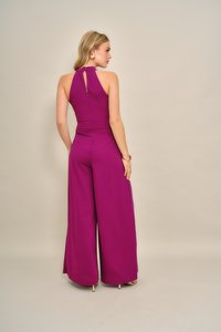 Fuksziaszínű overál hármas nyakú kialakítással, kivágott hátrésszel, széles szárakkal és sima, texturált anyagból. Látható díszgombos záródás.