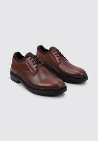 Zapatos de vestir de cuero marrón con textura suave, punta redondeada y suelas de goma negra. Presentan un diseño con cordones y un sutil detalle de costura.