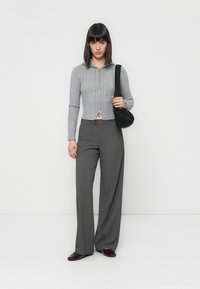 Felpa grigia corta con design a maglia cable, abbinata a pantaloni grigi a vita alta. Il modello tiene una borsa a tracolla nera. Scarpe marroni con lacci.