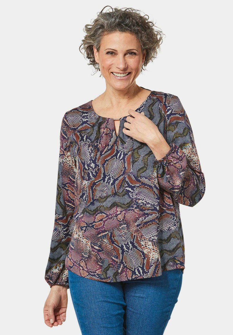 Langärmlige Bluse mit multicoloriertem abstraktem Muster. Sie hat einen runden Ausschnitt mit einer kleinen Schlüssellochöffnung und elastischen Manschetten.