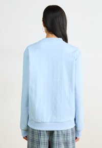 Sudadera azul claro con rayas verticales, cuello redondo y puños acanalados. Textura suave, combinada con pantalones de cuadros.