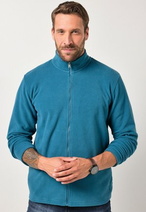 Chaqueta de forro polar en color teal con cuello alto, cremallera frontal completa y mangas largas. Presenta puños acanalados y un detalle de logo sutil en el dobladillo.