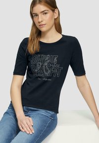 T-shirt en coton noir à manches courtes, à encolure ronde, avec un texte imprimé en blanc et argent, présentant des phrases motivantes.