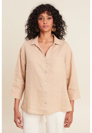 Chemise en lin beige avec col, fermeture à boutons, poche poitrine et manches trois-quarts. Présente une coupe légèrement ample et un détail à franges en bas.