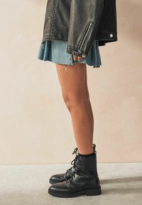 Sorte læder ankelstøvler med snørrebånd og rund tå, parret med en slidte denimnederdel. Sort læderjakke med sølvhardware detalje.