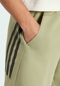 Světlé zelené sportovní šortky vyrobené z měkké tkaniny, s boční kapsou a třemi černými vertikálními pruhy podél levé strany.