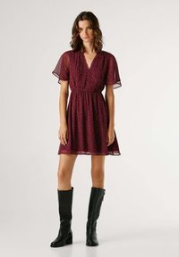 Vestido malva con lunares, mangas cortas con volantes, cintura ceñida y falda acampanada; combinado con botas de cuero negras hasta la rodilla.
