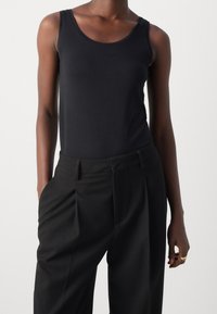 Černý bezrukávový top spojený s černými vysokými kalhotami s texturou. Top má kulatý výstřih a slim fit.