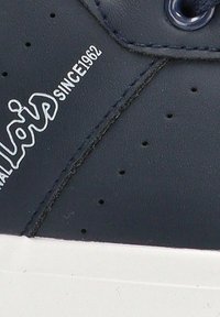 Zapatilla de cuero marino con perforaciones, suela de goma blanca y logo grabado "desde 1962" en el lateral. Textura suave y diseño minimalista.