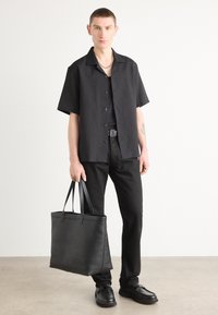 Camisa negra de manga corta, pantalones negros y bolso negro. El material parece suave; la camisa tiene cierre de botones; los zapatos presentan un diseño plano.
