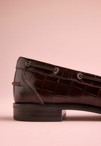 Mocasini burgundi din piele texturată cu model crocodil, prevăzuți cu ochiuri argintii și toc scăzut în stivă. Finisaj neted.