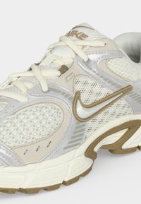 Άσπρο και μπεζ παπούτσι Nike για τρέξιμο με διχτυωτές επιφάνειες, παχιά σόλα και κλείσιμο με κορδόνια, τονίζοντας το λογότυπο Nike swoosh στο πλάι.