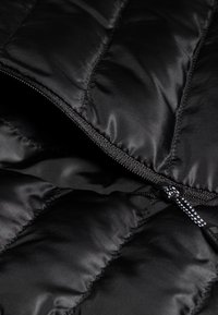 Zwarte pufferjack binnenzijde met gequiltte secties. Heeft een gladde nylon textuur en een rits met een contrasterende trekband.