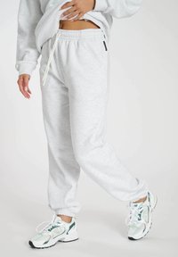 Hellgraue Sweatpants aus weichem Material mit elastischem Bund und Bündchen, ausgestattet mit einem weißen Kordelzug und einem kleinen schwarzen Etikett.