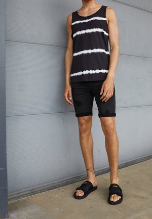 Sort tanktop med hvide horisontale striber, paired med slidte sorte denimshorts og sorte sandaler med et enkelt spænde-design.