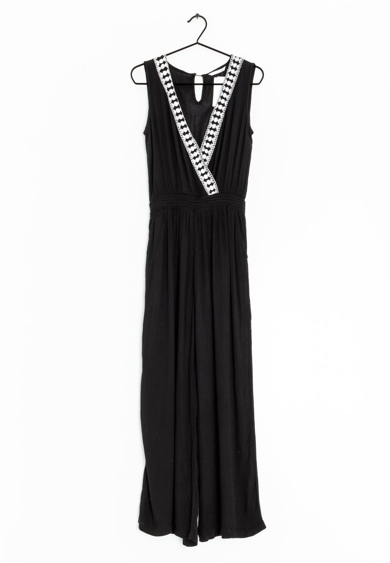 Combinaison noire sans manches avec jambes larges, encolure en V profonde ornée de détails blancs à motifs, suspendue sur un cintre noir.