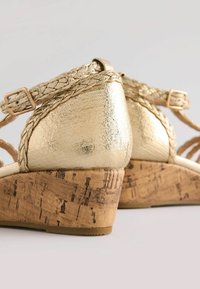 Goldene, metallische Wedgesandalen mit geflochtenen Riemen, Korkabsatz, strukturiertem Obermaterial und Schnallenverschluss. Auffällige Form für Stabilität und Stil.