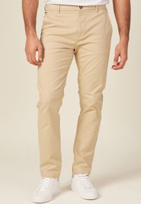Chinos beige hechos de una tela ligera, con un corte recto y sutiles bolsillos laterales, combinados con zapatillas blancas.