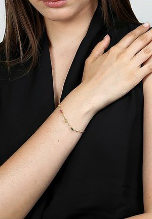 Goldene Kettenarmband mit bunten Edelsteinen. Zartes Design mit grünen, rosa und klaren Akzenten. Wird an einem nackten Handgelenk getragen.