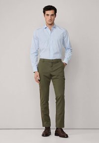 Svetlomodrá pruhovaná košeľa na gombíky s dlhými rukávmi, doplnená olivovo zelenými cargo nohavicami. Outfit dopĺňajú hnedé topánky.