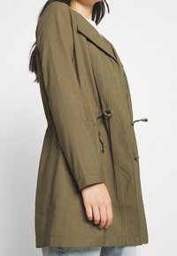Olive green lightweight jacket with a wide collar, drawstring waist, and button details. Smooth texture and long sleeves.