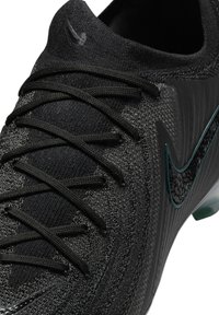 Scarpa da calcio nera con tomaia testurizzata, design elegante, lacci prominenti e logo swoosh nero con accenti verdi sul lato.