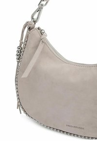 Borsa beige in suede con una forma curva, hardware in tonalità argento e dettagli borchiati lungo il bordo. Presenta una chiusura a zip e nappine decorative.