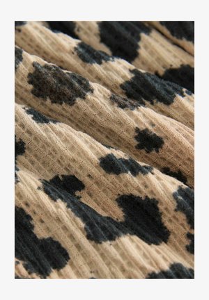 Tekstilstof med en beige baggrund og sorte plettede mønstre, der viser en struktureret, ribbet overflade.