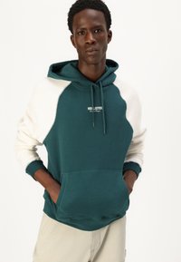 Teal and cream color-blocked hoodie with a front pocket, adjustable drawstring, and 'Hollister' logo. Soft, textured cotton fabric.