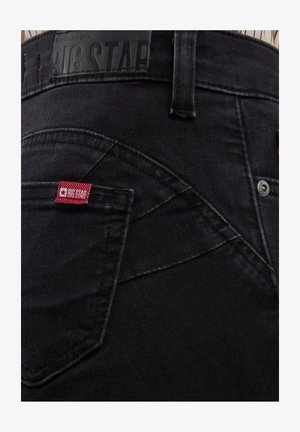 Detaljan prikaz stražnjeg džepa crnih traperica s crvenom tkanom oznakom "BIG STAR" i crnim kožnim logom na pojasu.