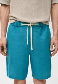 Shorts turchesi realizzati in un tessuto leggero, con un elastico in vita e un cordino beige. Texture liscia, taglio a lunghezza ginocchio.