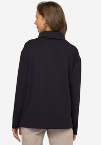 Pullover lungo nero a maniche lunghe con collo alto, vestibilità rilassata, texture morbida e spacchi laterali all'orlo. La vista posteriore mostra cuciture delle spalle arrotondate.