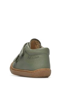 Scarpa per bambini in morbida pelle verde chiaro, con un cinturino in Velcro, forma arrotondata e suola in gomma testurizzata di colore marrone chiaro.