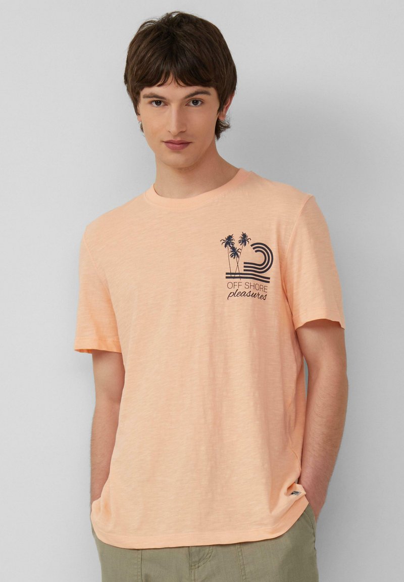 Perzikkleurig katoenen T-shirt met korte mouwen. Bevat een bedrukte afbeelding van palmbomen en golven op de linkerkant van de borst. Zachte textuur.